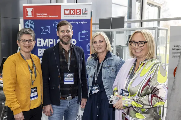 2024: Vier Personen mit Namensschildern lächeln vor einem Messestand beim eDay Salzburg.
