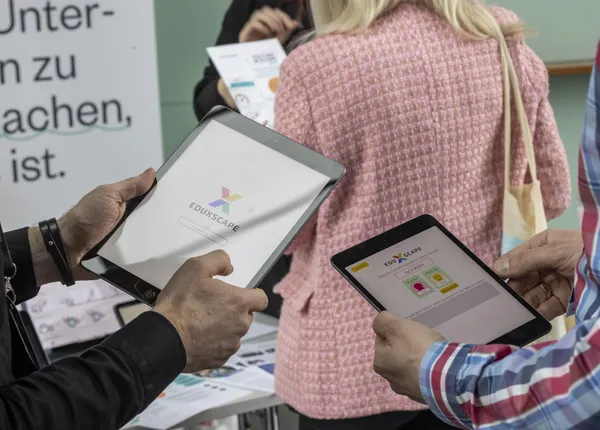 2024: Hände halten Tablets mit App-Demos am Ausstellerstand beim eDay Salzburg.