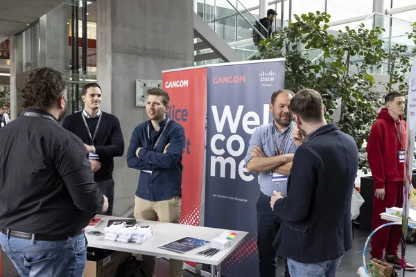 2024: Ausstellerinnen und Aussteller am Messetisch mit Welcome-Banner im Foyer beim eDay Salzburg.