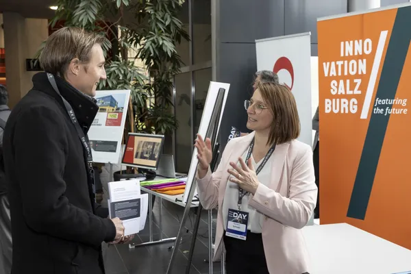 2024: Mitarbeiterin erklärt einem Besucher Angebote am Innovationsstand beim eDay Salzburg.
