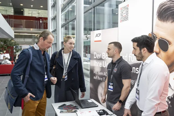 2024: Gespräch an einem Ausstellerstand (ACP) mit Laptop zwischen Besuchern und Personal.