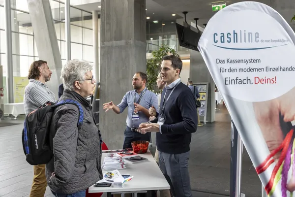 2024: Standpersonal erklärt ein Produkt am Ausstellerstand mit 'cashline'-Banner.