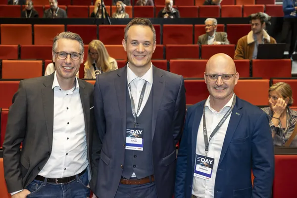 2024: Drei Personen mit eDay-Badges im Vortragssaal vor roten Sitzen.