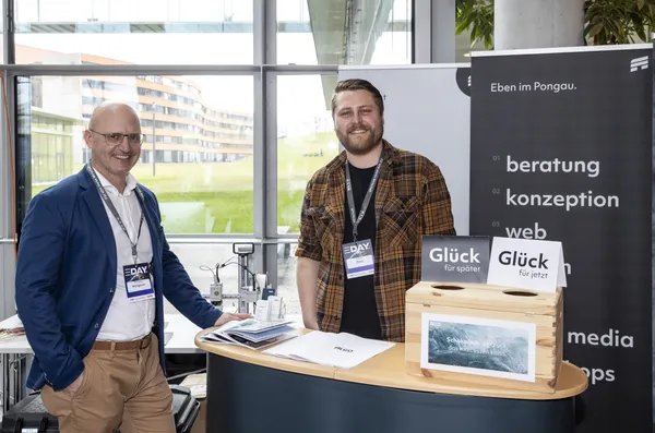 2024: Zwei Personen an einem Ausstellerstand mit 'Glück'-Schildern.