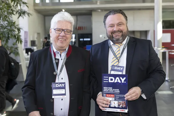 2025: Zwei Personen mit eDay-Badges und Flyer in der Eingangshalle.