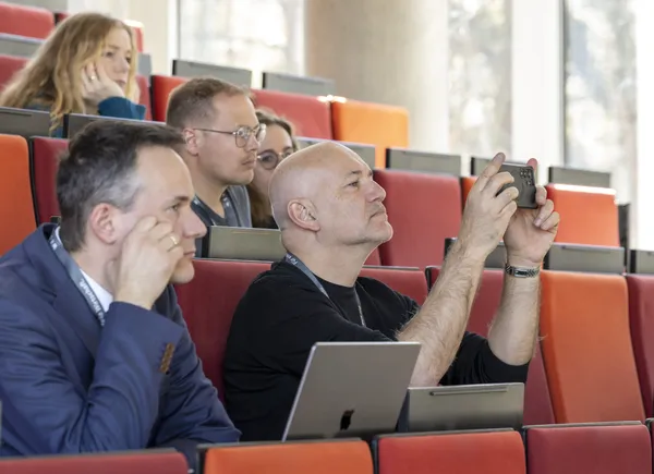 2025: Teilnehmer fotografiert mit Smartphone aus dem Publikum im Hörsaal beim eDay Salzburg.