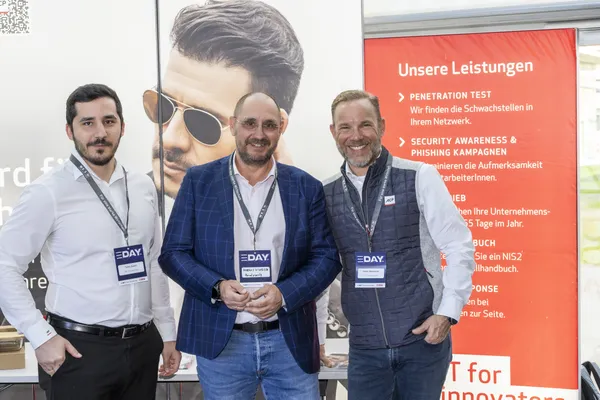 2025: Drei Personen am Messestand vor Werbebanner mit Leistungen stehen bereit beim eDay Salzburg.