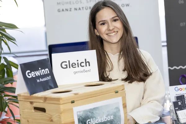 2025: Frau lächelt an Gewinn-Box mit Schild 'Gleich genießen!' am Stand beim eDay Salzburg.