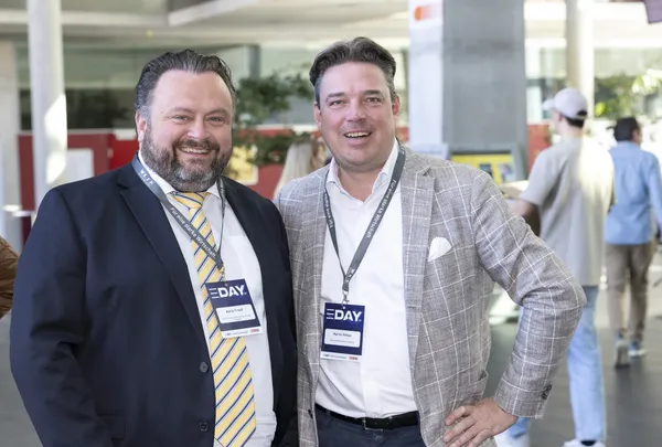 Zwei Männer in Anzügen mit E‑DAY-Badges stehen lächelnd im Foyer beim eDay Salzburg 2025