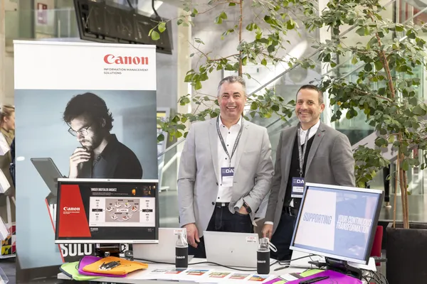 Zwei Aussteller am Canon-Stand mit Monitoren und Prospekten beim eDay Salzburg 2025