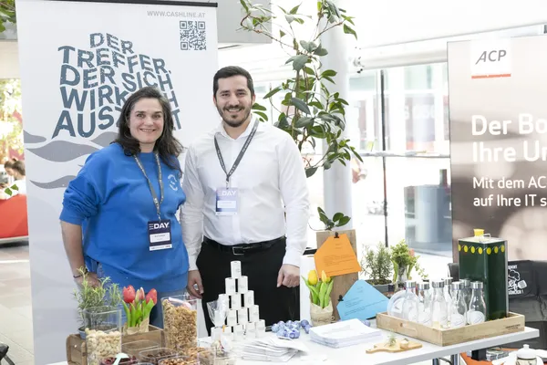 Zwei Aussteller am Messetisch mit Flyern und Giveaways beim eDay Salzburg 2025