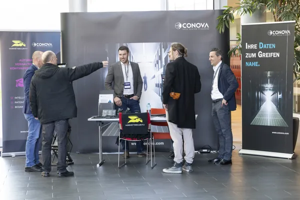 Gruppe führt Gespräch vor CONOVA-Stand mit Bannern beim eDay Salzburg 2025