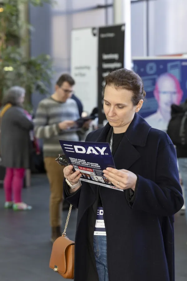 Teilnehmerin liest Programmheft 'E‑DAY' im Foyer beim eDay Salzburg 2025