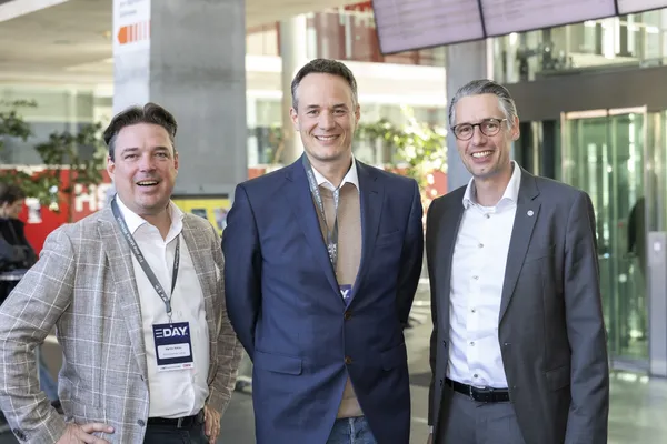 Drei Männer mit E‑DAY-Badges lächeln in der Eingangshalle beim eDay Salzburg 2025