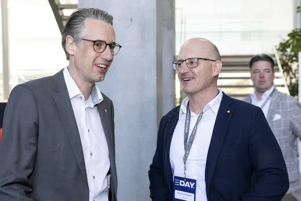 Zwei Männer im Gespräch mit E‑DAY-Badges im Foyer beim eDay Salzburg 2025