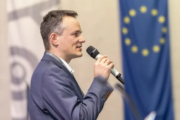 Seitliches Porträt eines Vortragenden mit Mikrofon und EU-Flagge im Hintergrund beim eDay Salzburg 2025.
