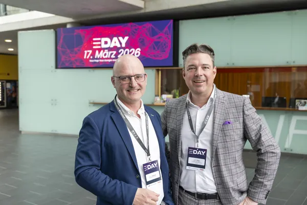 Zwei Personen mit Badge vor Bildschirm mit eDay 17. März 2026 im Foyer beim eDay Salzburg 2026.