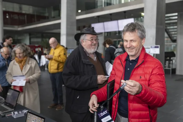 Personen im Foyer beim eDay Salzburg 2026, Vordergrund Mann mit roter Jacke und Badge.