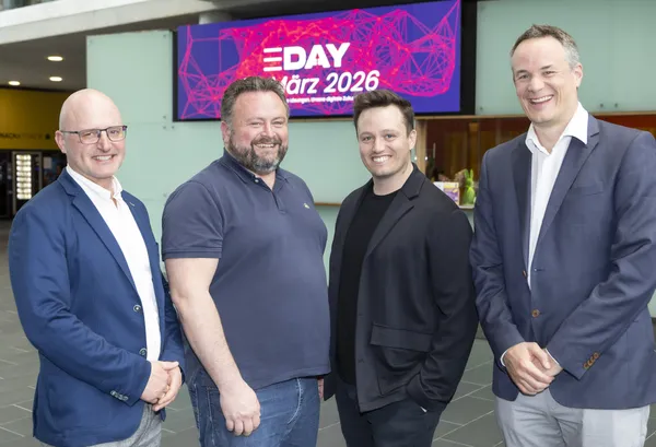Vier Personen stehen lächelnd vor E‑DAY-Banner 'März 2026' in der Empfangshalle beim eDay Salzburg 2026.