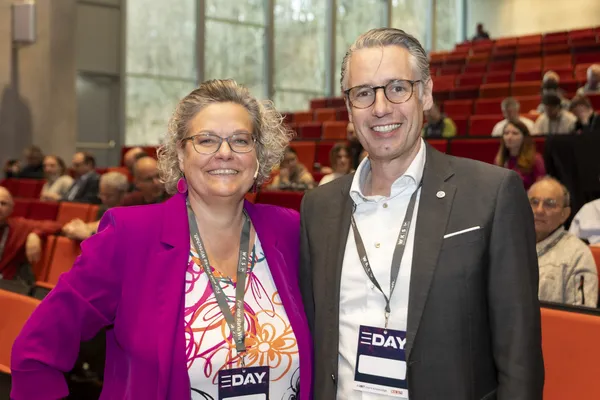 2026: Zwei Personen mit Namensschildern posieren vor dem Publikum im Saal beim eDay Salzburg.