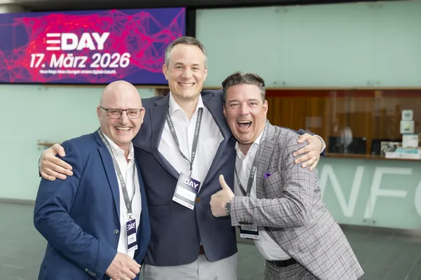 2026: Drei Männer posieren lächelnd vor dem Empfangsbereich beim eDay Salzburg.