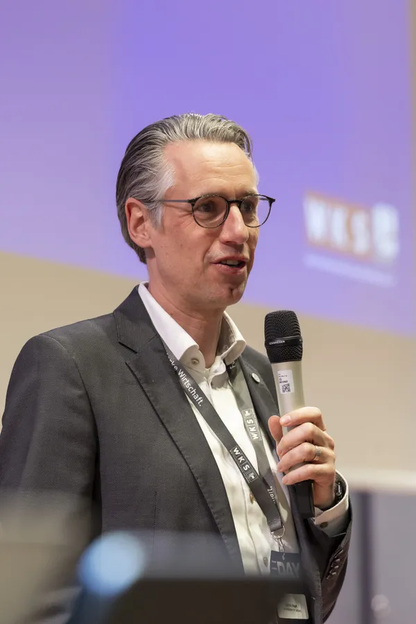 2026: Sprecher im Anzug mit Mikrofon vor projiziertem WKS-Logo beim eDay Salzburg.